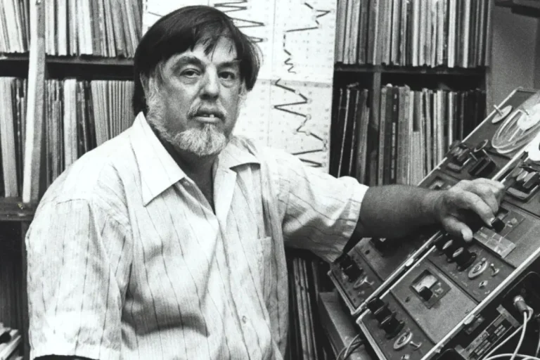 Alan Lomax standing beside vintage audio recording equipment.