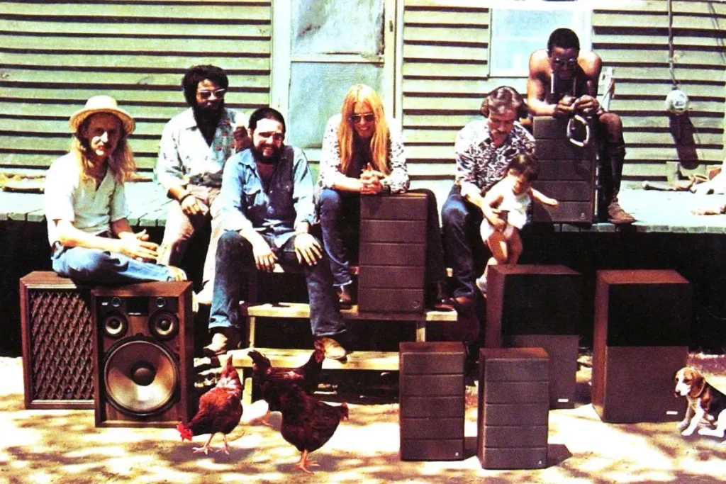Allman Brothers Band members seated outdoors with speakers and instruments.