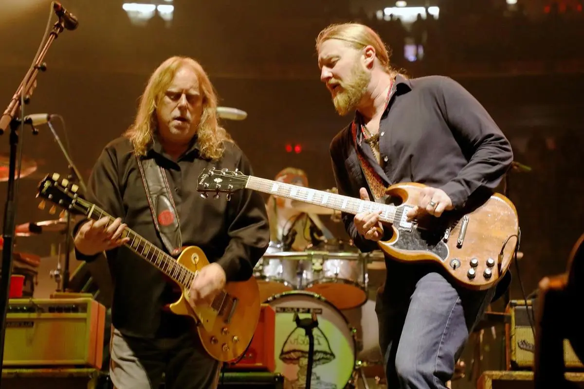Allman Brothers perform onstage side by side, intensely focused as they play their electric guitars under warm stage lighting.