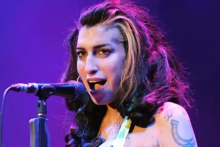Amy Winehouse singing into a microphone under purple stage lighting.