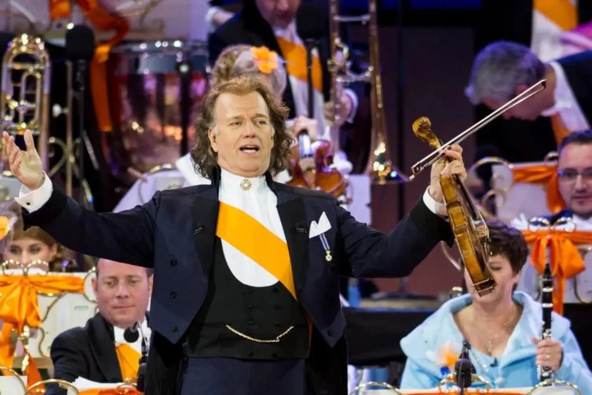 André Rieu standing center stage with arms open.