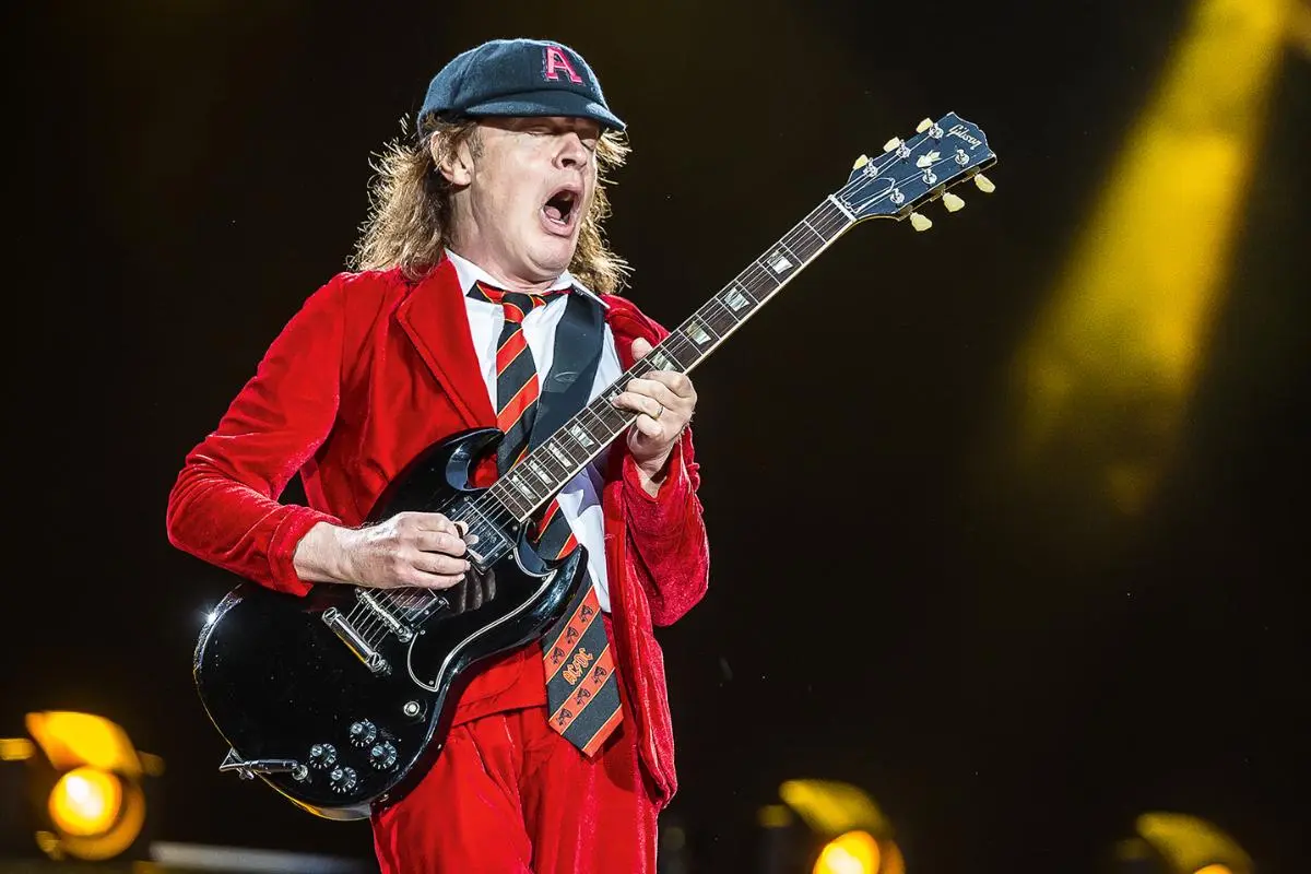 Angus Young guitarist performing on stage in a red schoolboy outfit.