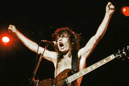 Angus Young performing shirtless on stage with arms raised and an electric guitar.