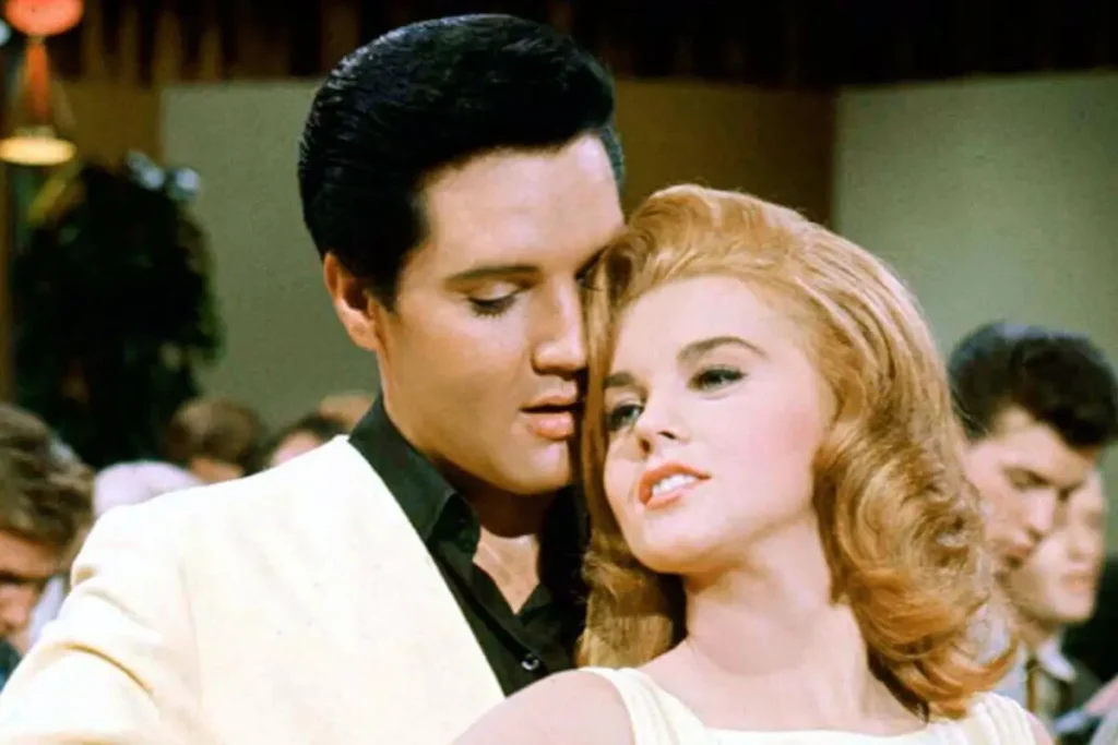 A Elvis Presley in a light suit leans close to Ann-Margret with styled hair on a dance floor, creating an intimate, cinematic moment.