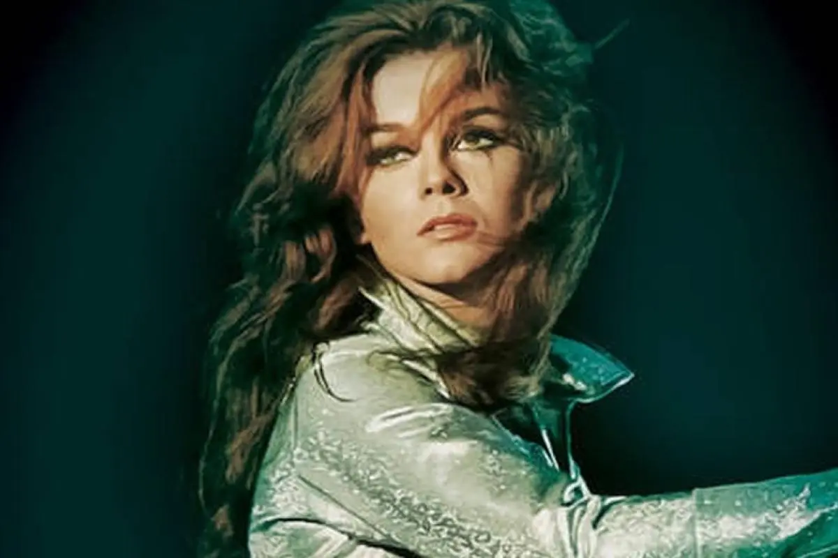   Ann-Margret with dramatic eye makeup and flowing hair looks over her shoulder under stage lighting, wearing a shimmering outfit.