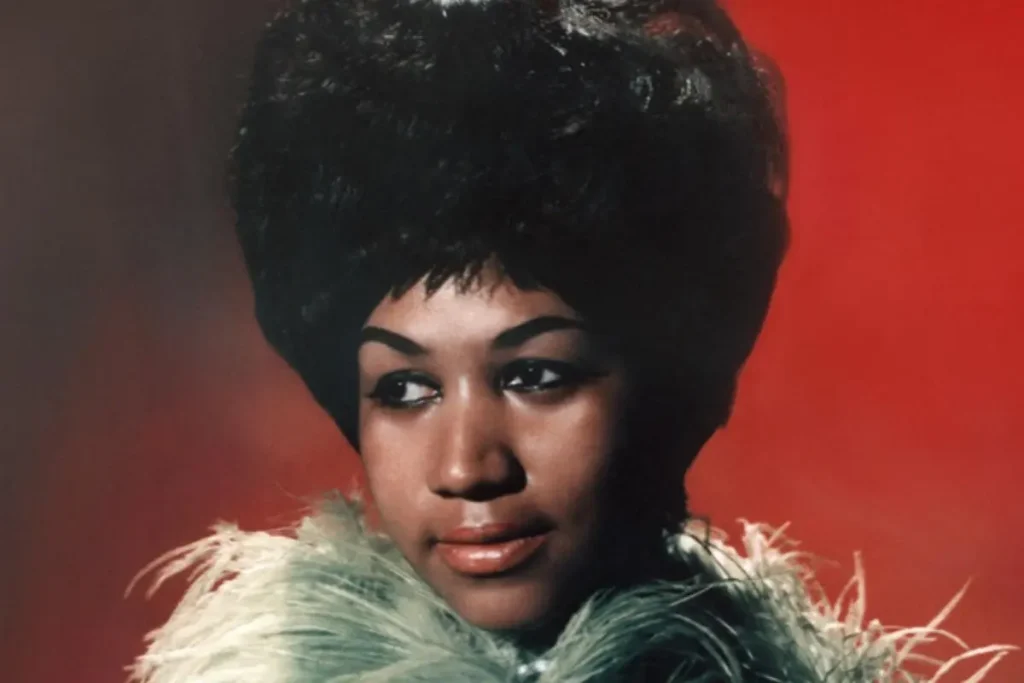 Portrait of Aretha Franklin wearing a green feathered outfit against a red background.