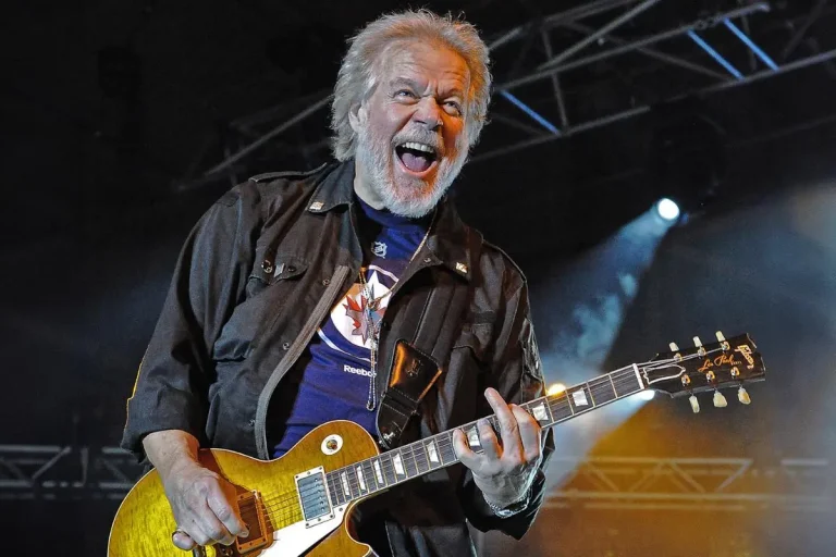 Billy Gibbons smiling broadly while playing a gold-top electric guitar.