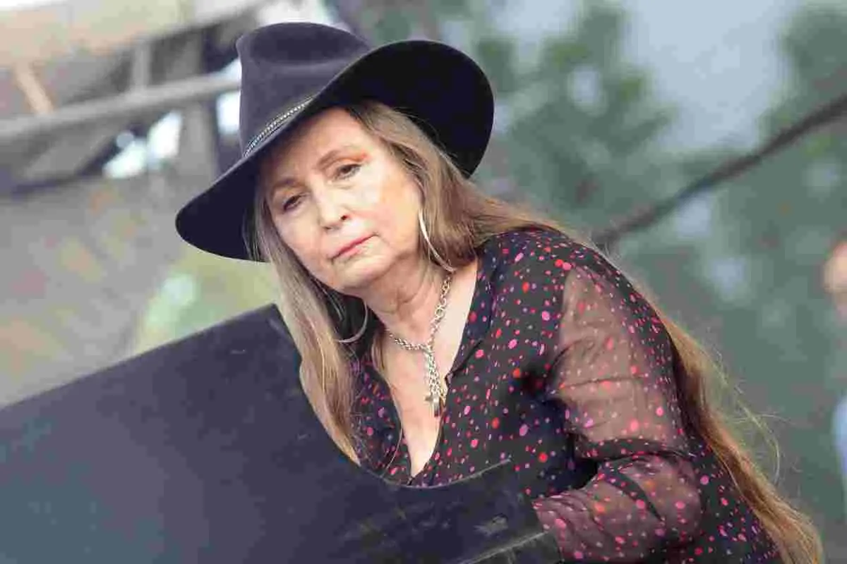 Bobbie Nelson performing on stage at a piano, wearing a black hat and patterned blouse under soft stage lighting.