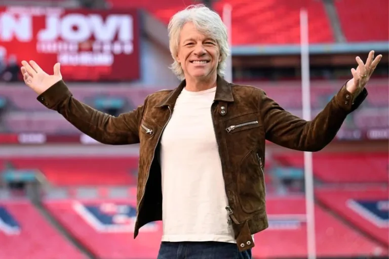 Jon Bon Jovi smiling with arms open in a football stadium.