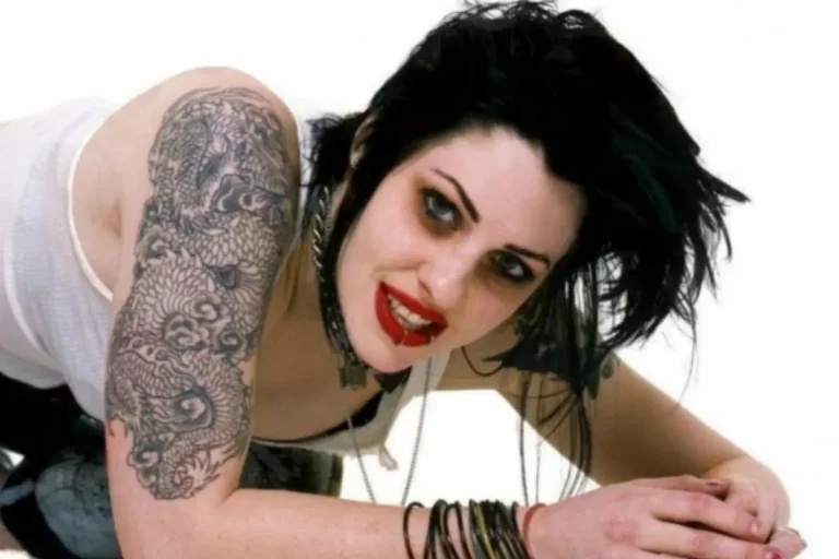 Portrait of Brody Dalle leaning forward with black hair and tattooed arm.