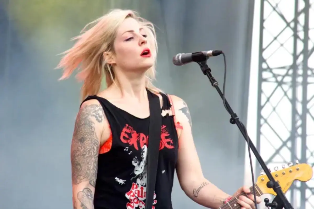 Brody Dalle singing into a microphone while playing guitar on stage.