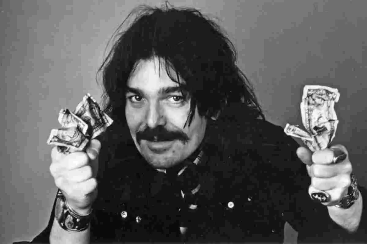 Jeff Beck performing on stage, singing into a microphone in a black vest.