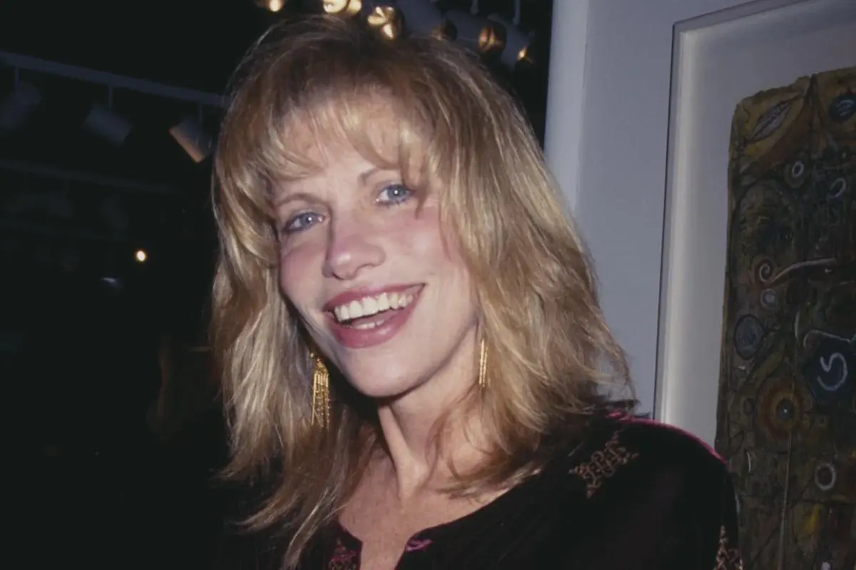 Carly Simon smiling at an indoor event, wearing earrings and a dark top.