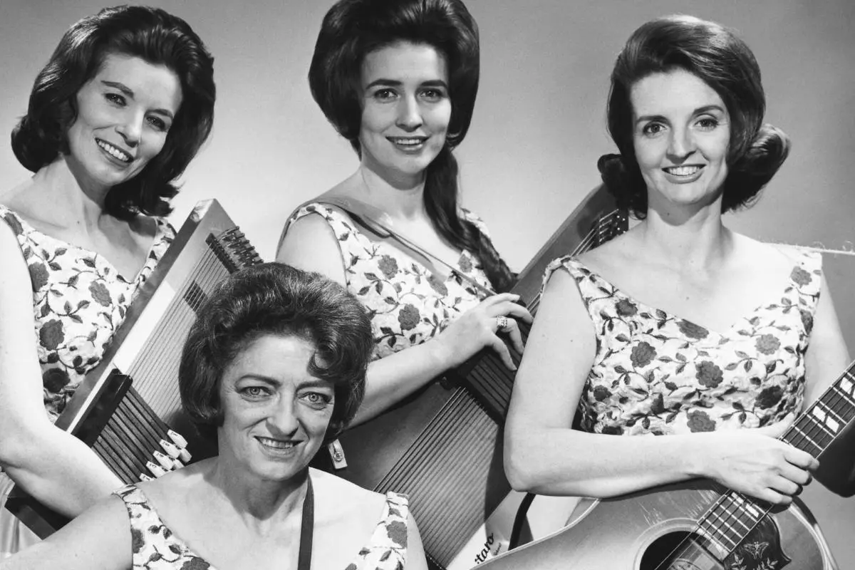 Carter Family pose with guitars and autoharps, smiling in matching floral dresses in a studio portrait.
