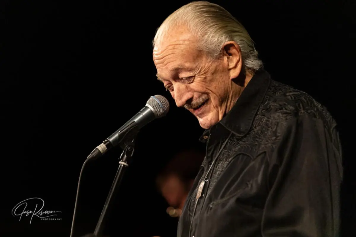 Charlie Musselwhite smiling at a microphone during a live performance.