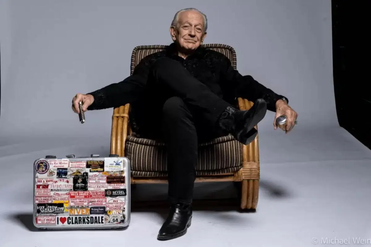 Portrait of Charlie Musselwhite seated in a chair holding harmonicas.