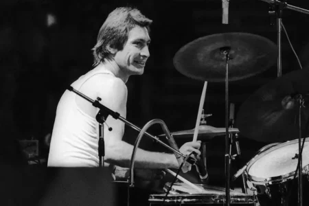 Charlie Watts performing live on drums in a black-and-white photo.