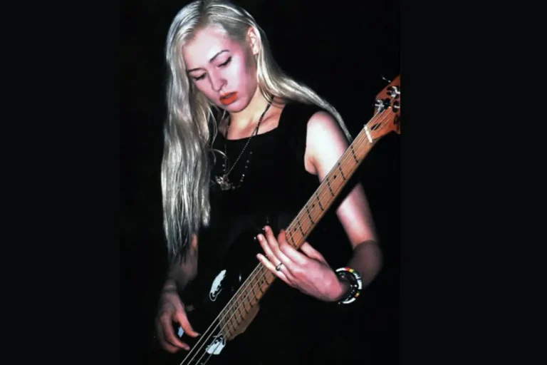 D’arcy Wretzky blonde bassist performing onstage under dark lighting.