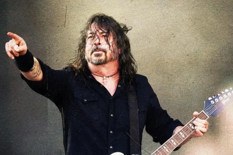 Dave Grohl performing onstage, pointing toward the crowd while playing electric guitar.