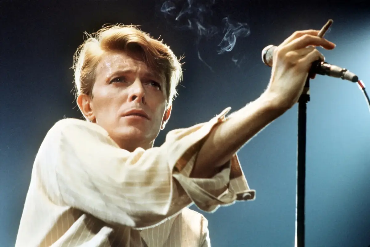 David Bowie on stage holding a microphone under dramatic lighting, capturing intensity, focus, and emotional connection during a live performance.
