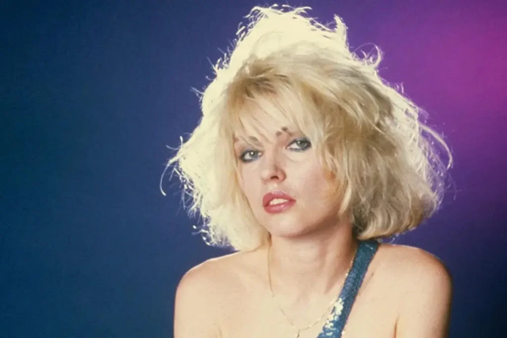 Debbie Harry with tousled hair, gazing forward against a blue and purple backdrop.