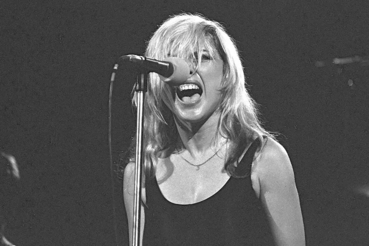 Black-and-white image Debbie Harry shouting into a microphone during a live concert.