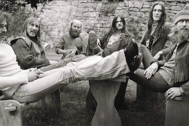Deep Purple members relaxing outdoors, seated casually around stone stools in a black-and-white photo.