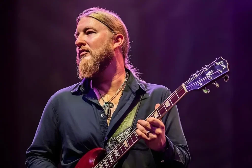 Derek Trucks on stage holding an electric guitar, emphasizing concentration, artistry, and the expressive nature of live music.