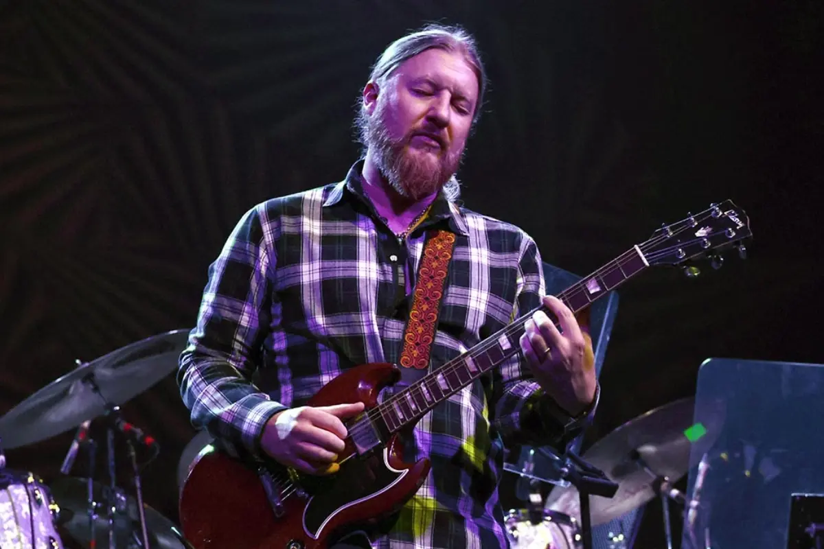 Derek Trucks performing on stage with a slide guitar under concert lighting, conveying focus, precision, and emotional expression during a live performance.