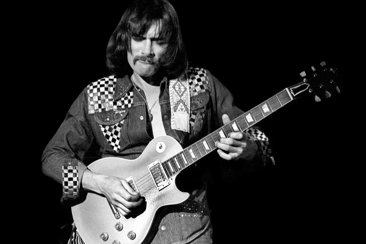 Dickey Betts playing electric guitar in a black and white concert photo.