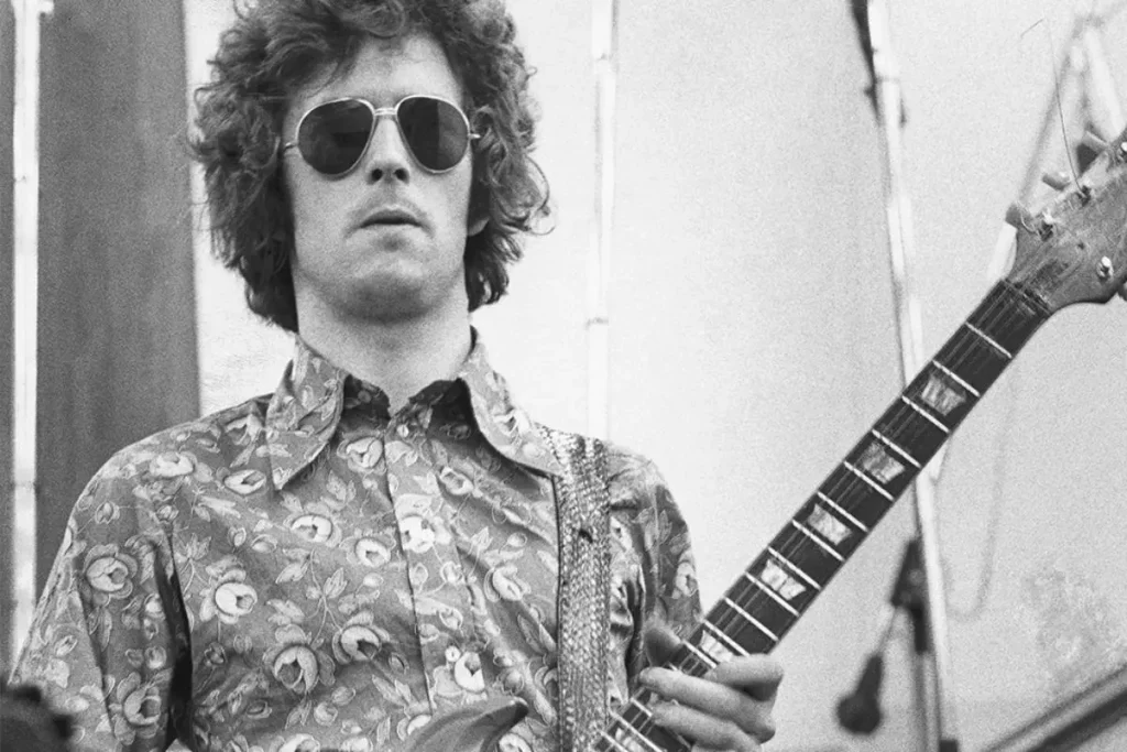 Clapton wearing sunglasses and playing an electric guitar onstage.