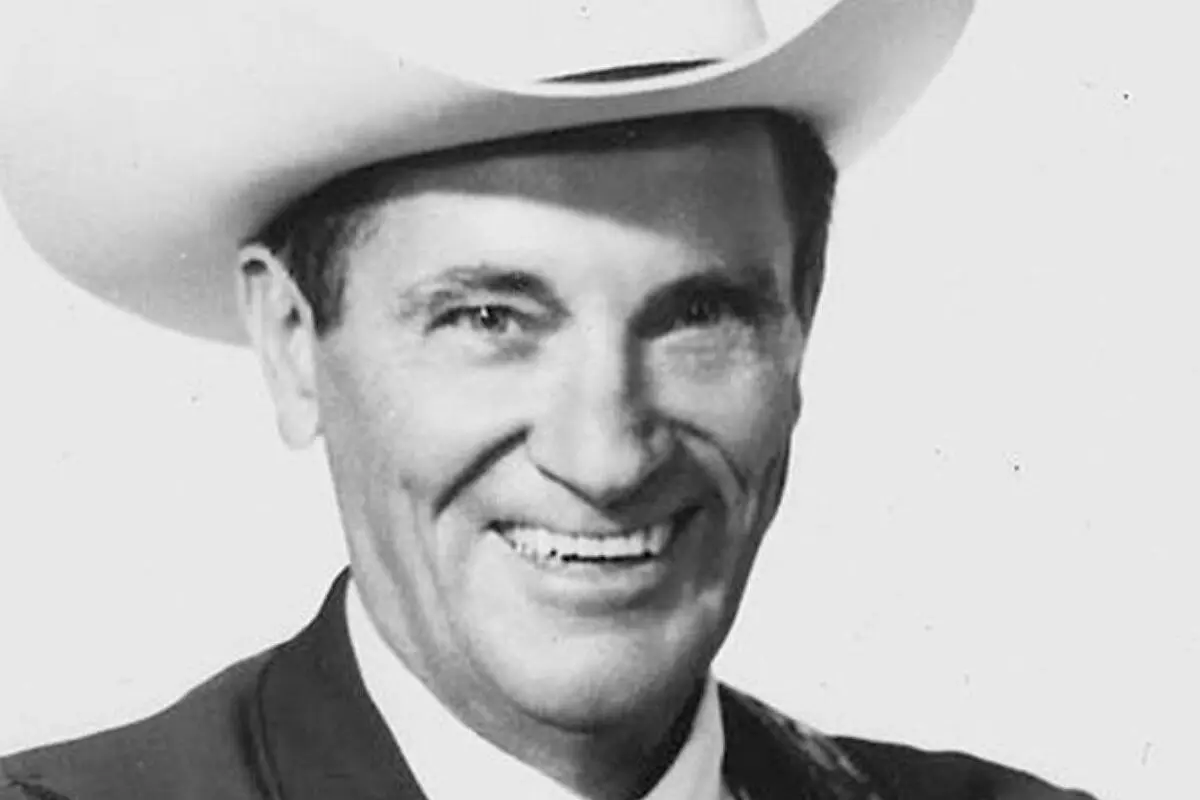 Ernest Tubb smiling, wearing a white cowboy hat and suit jacket against a plain background.