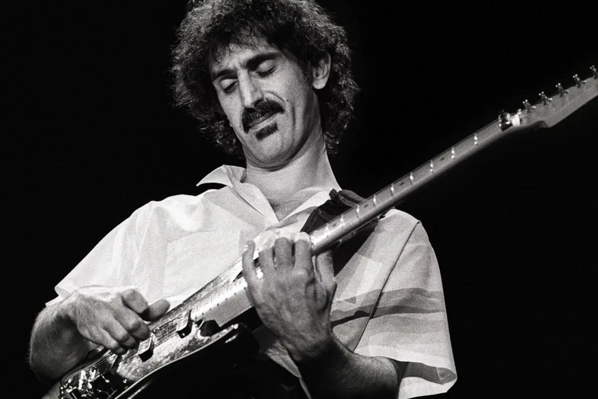 Frank Zappa close-up of a curly-haired guitarist with a mustache, eyes closed while playing an electric guitar during a live performance.