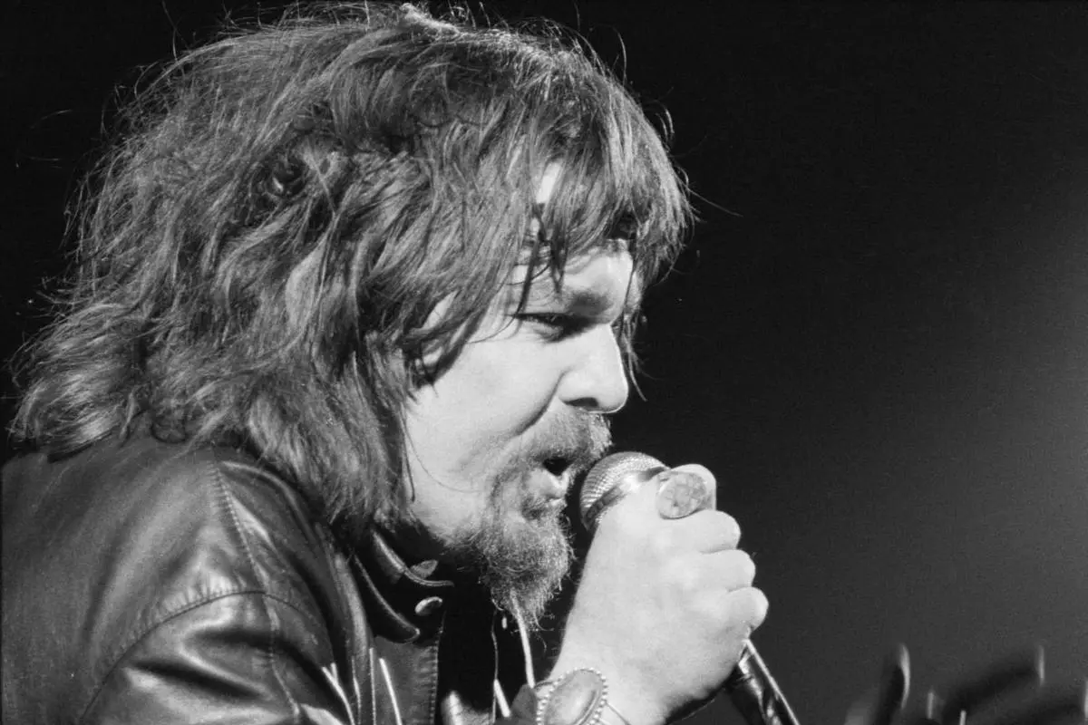 Frank in a leather jacket singing into a handheld microphone.