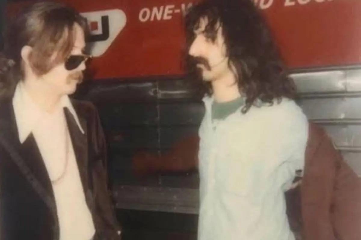 Frank and Eric standing face-to-face near a tour bus, appearing to talk backstage.