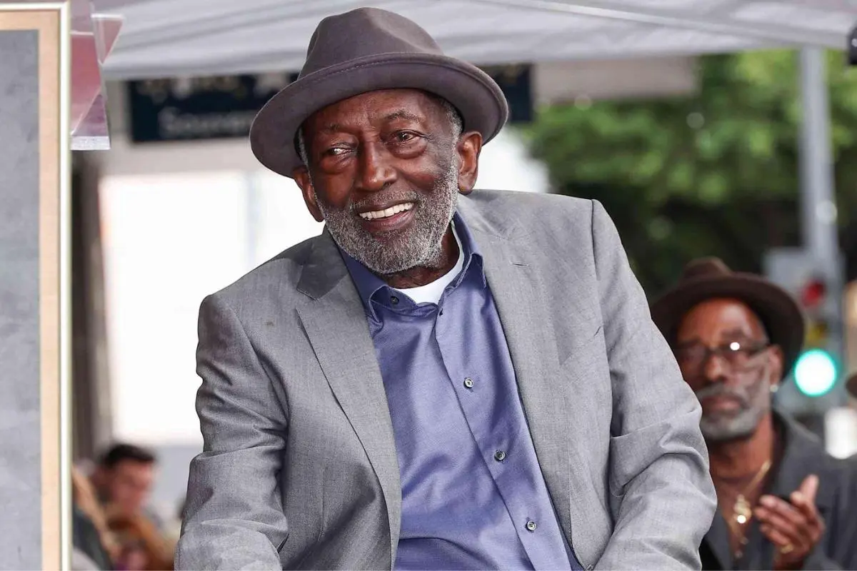 Garrett Morris smiling at an outdoor event wearing a gray suit and hat.