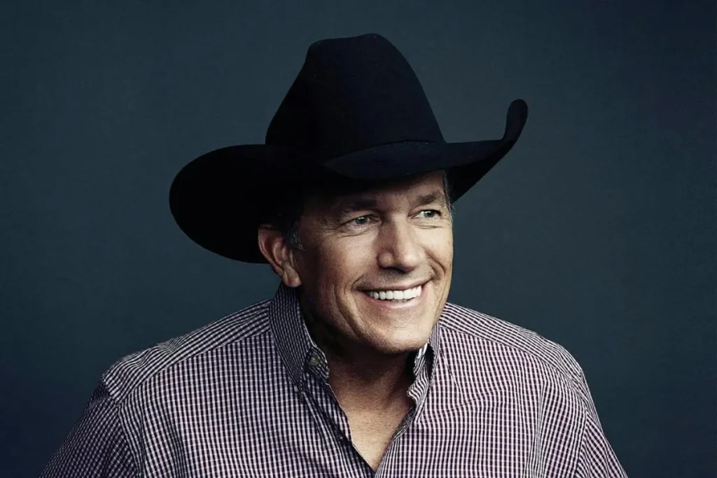 George Strait studio portrait, wearing a black cowboy hat and checkered shirt, smiling.