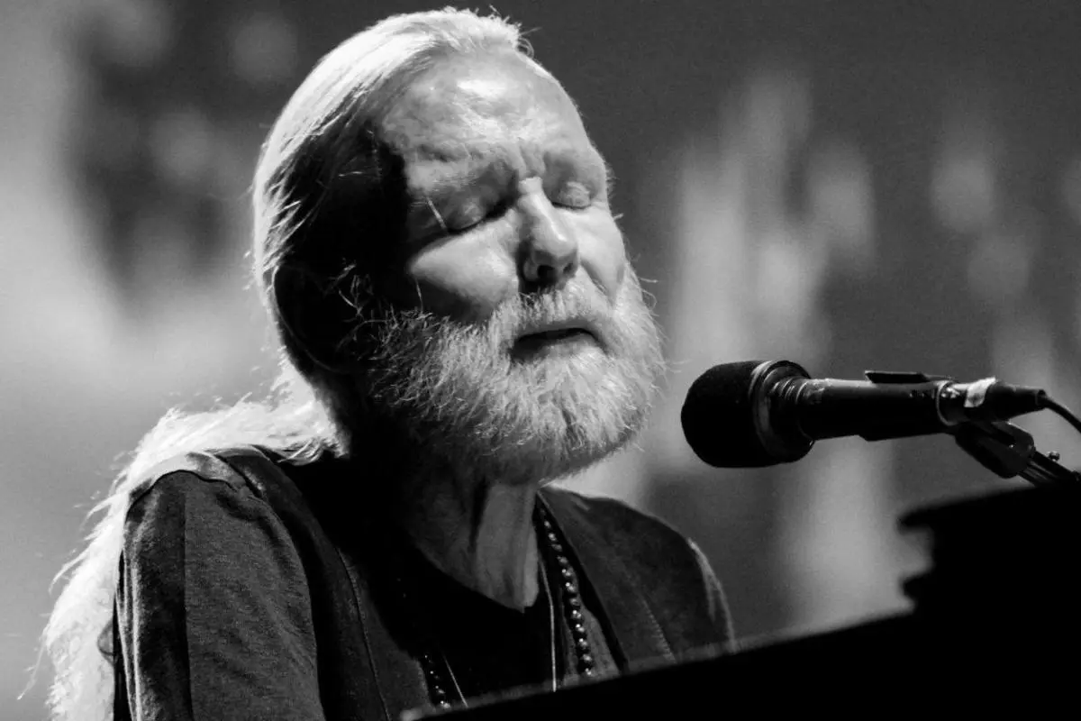 Gregg Allman, eyes closed in concentration, sings into a microphone under dramatic monochrome lighting during a soulful performance.