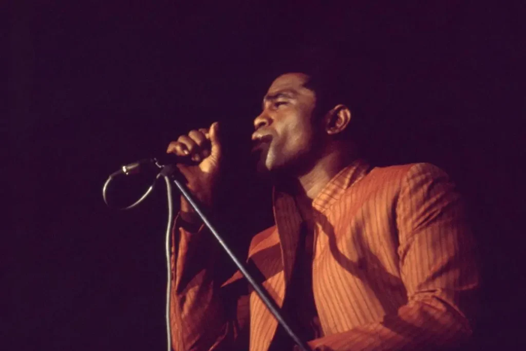 James Brown performing live on stage, singing passionately into a microphone.