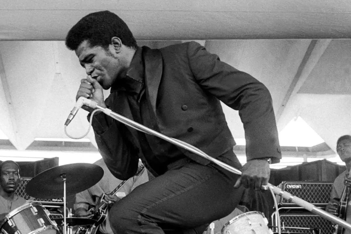 James Brown delivering an intense live performance, leaning forward with signature stage presence.