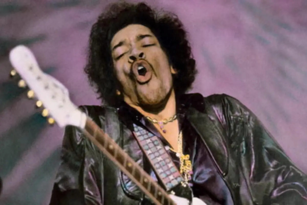 Jimi Hendrix performing live on stage, singing while playing electric guitar.