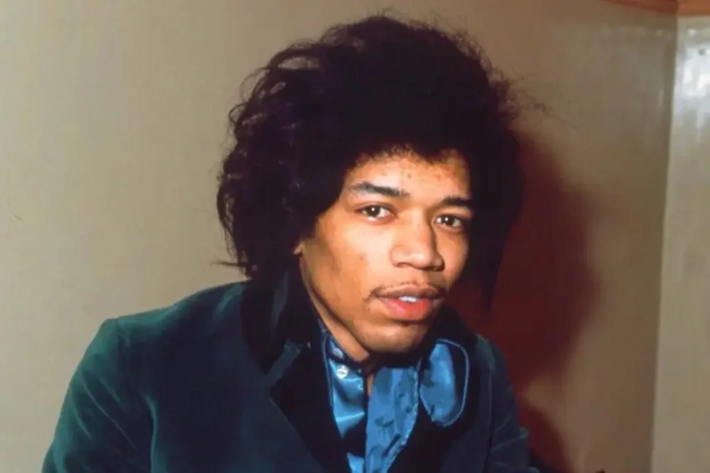 Portrait of Jimi Hendrix wearing a blue shirt and dark jacket indoors.