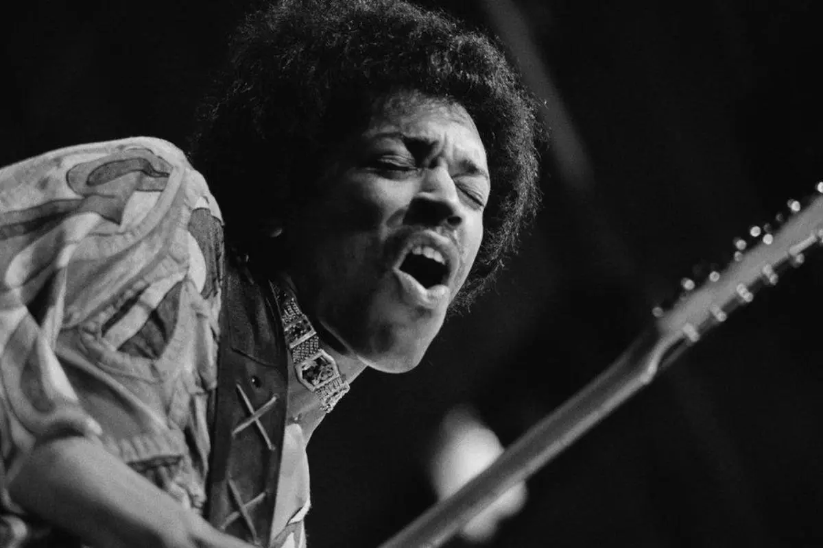 Jimi Hendrix singing passionately while playing electric guitar, black-and-white performance photo.