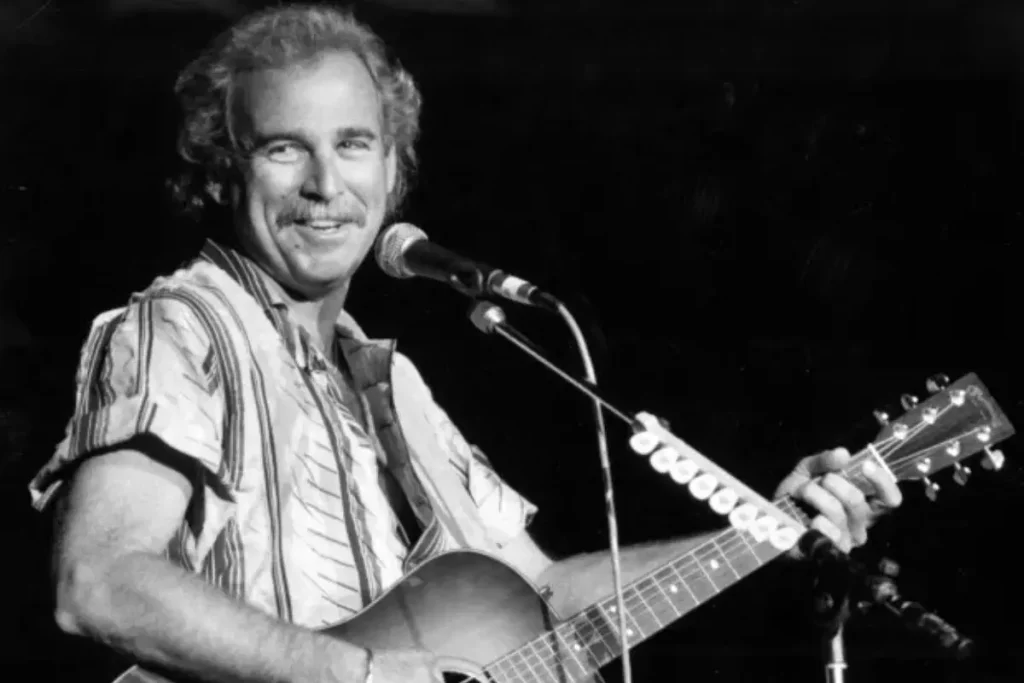 Jimmy Buffett smiling while performing with an acoustic guitar on stage.
