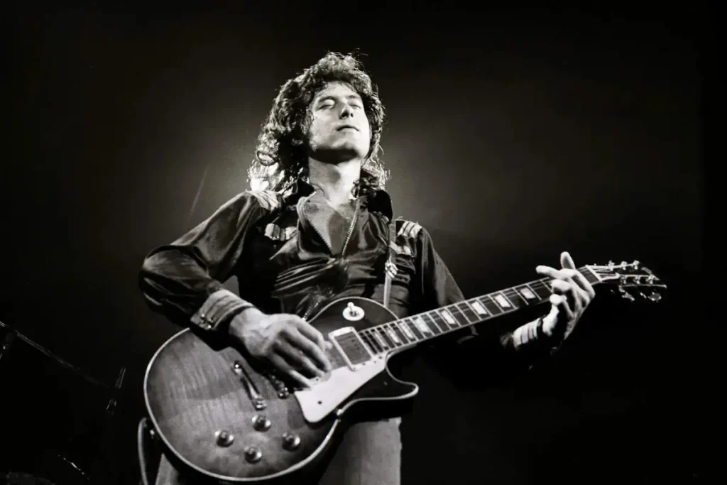 Jimmy Page performing on stage with an electric guitar in a dramatic black-and-white concert photo.
