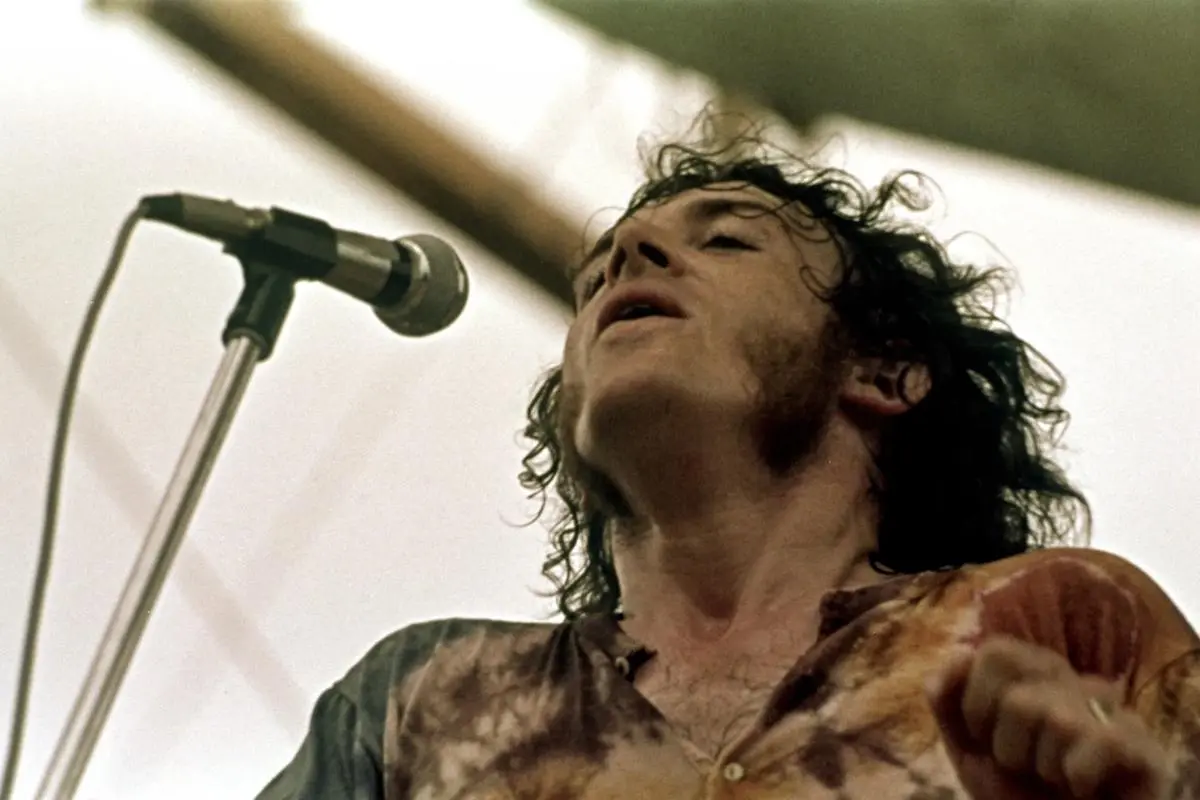 Joe Cocker singing into a microphone during a live performance, head tilted back.