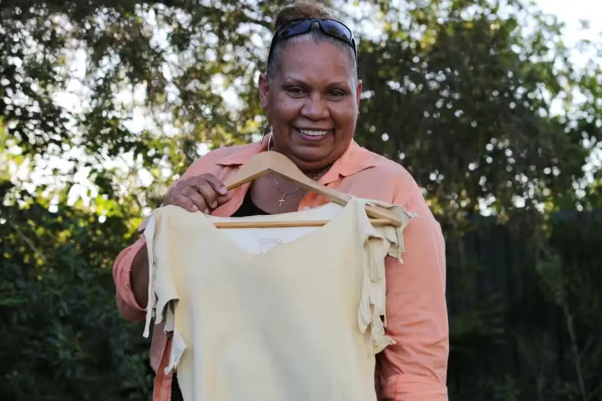 Joelene King holds up a sleeveless cream-colored top on a hanger.
