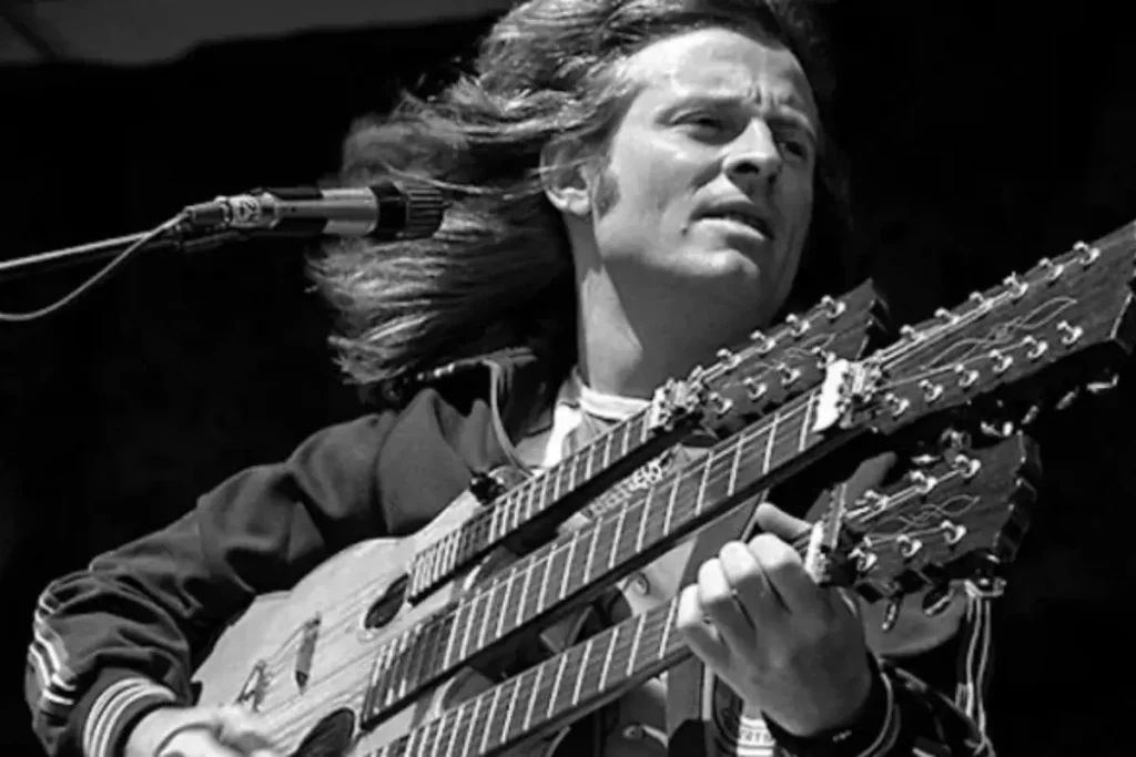 John Paul Jones performs onstage, playing a double-neck guitar while singing into a microphone.