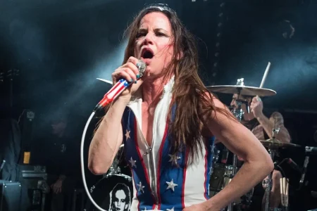Juliette Lewis on Warped Tour: ‘Bearded Lady’ Outsider to Muscular Rock Frontwoman Juliette Lewis performs onstage, singing into a microphone while wearing a sleeveless stars-and-stripes bodysuit.
