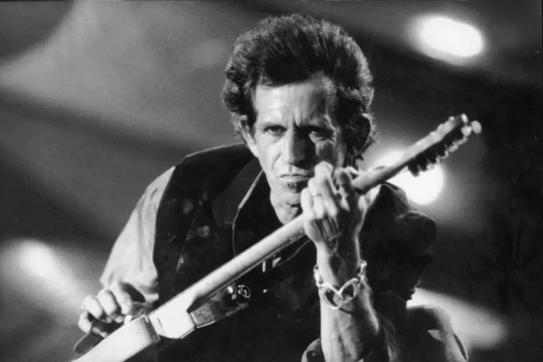 Keith Richards playing an electric guitar onstage, captured in a dramatic black-and-white close-up.